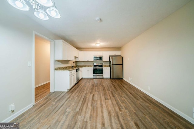 kitchen featuring light stone countertops, appliances with stainless steel finishes, sink, white cabinets, and hardwood / wood-style floors