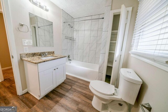 full bathroom featuring tiled shower / bath combo, wood-type flooring, a textured ceiling, toilet, and vanity