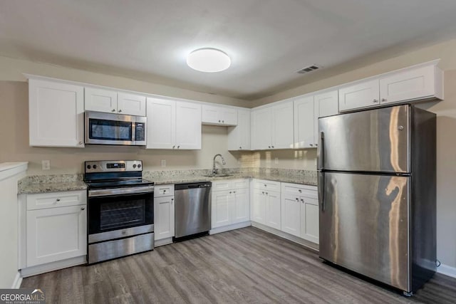 kitchen featuring white cabinetry, sink, light stone countertops, light hardwood / wood-style floors, and appliances with stainless steel finishes