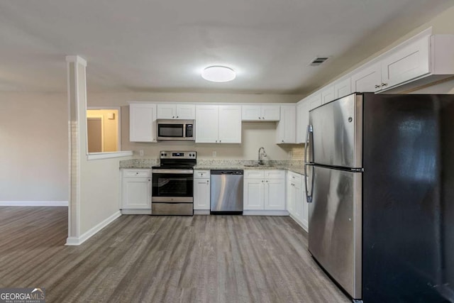 kitchen with light stone countertops, white cabinetry, sink, appliances with stainless steel finishes, and light wood-type flooring