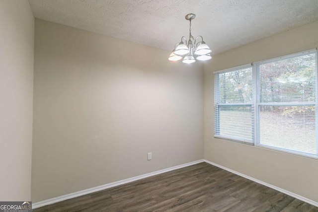 empty room featuring dark wood-type flooring, plenty of natural light, a chandelier, and a textured ceiling