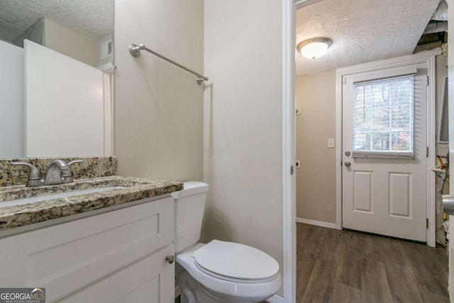 bathroom with hardwood / wood-style flooring, vanity, toilet, and a textured ceiling