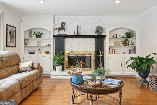 living room featuring ornamental molding, built in features, light hardwood / wood-style flooring, and a brick fireplace