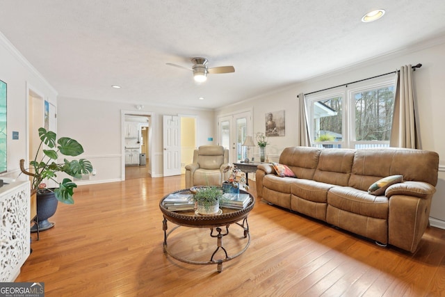 living room featuring a textured ceiling, light wood-type flooring, ceiling fan, and ornamental molding