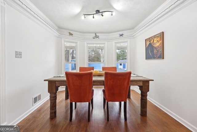 dining room with dark hardwood / wood-style floors, a textured ceiling, and ornamental molding