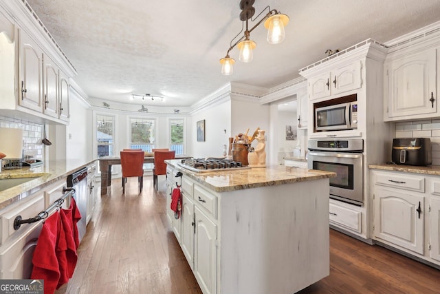 kitchen featuring a center island, backsplash, decorative light fixtures, white cabinetry, and stainless steel appliances