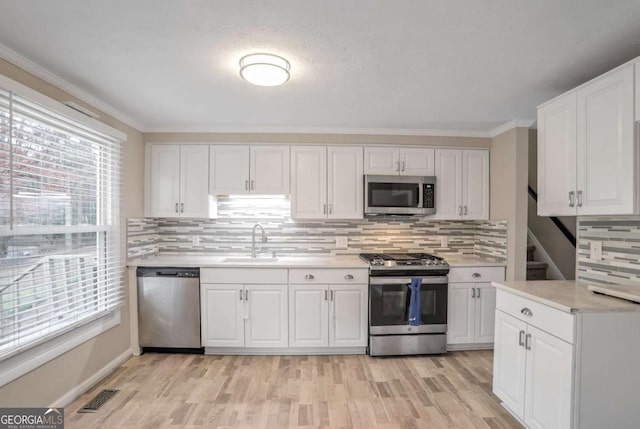 kitchen with backsplash, ornamental molding, stainless steel appliances, sink, and white cabinetry