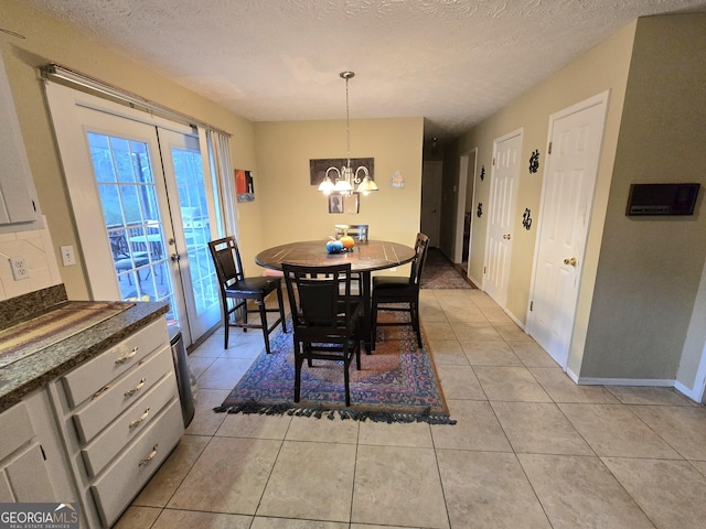 tiled dining area with french doors, a textured ceiling, and an inviting chandelier