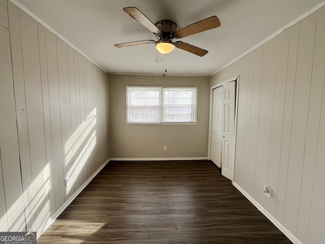 unfurnished bedroom featuring a closet, wooden walls, ceiling fan, dark hardwood / wood-style flooring, and ornamental molding