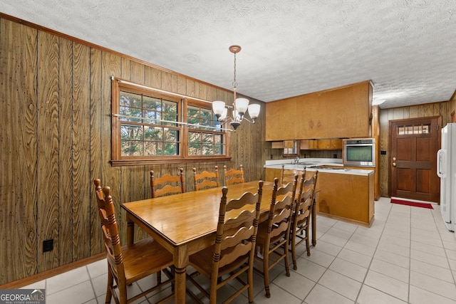 dining area featuring an inviting chandelier, light tile patterned floors, wooden walls, and a textured ceiling