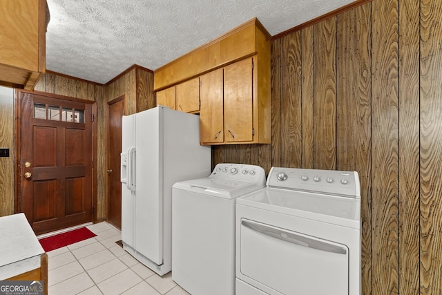 clothes washing area featuring wood walls, crown molding, cabinets, light tile patterned floors, and washing machine and dryer