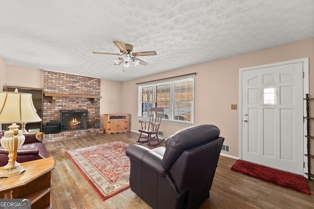 living room featuring a brick fireplace, hardwood / wood-style flooring, a textured ceiling, and ceiling fan