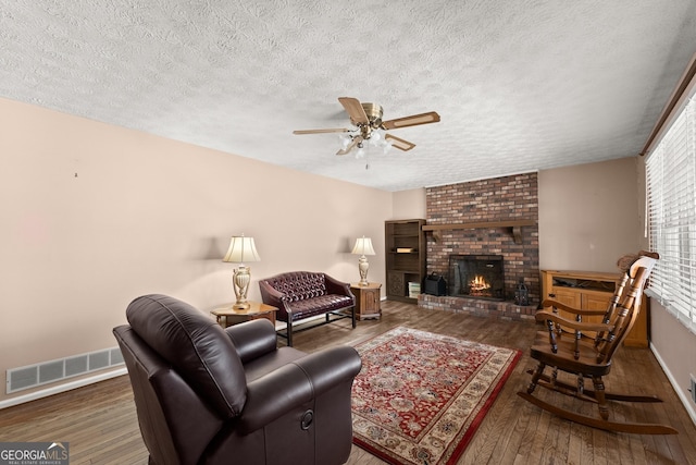 living room with ceiling fan, a brick fireplace, dark hardwood / wood-style floors, and a textured ceiling