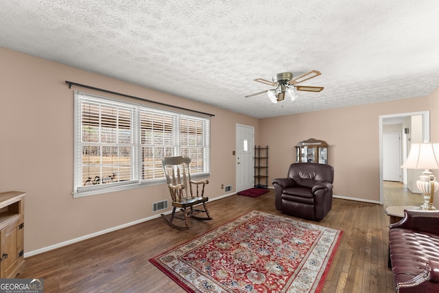 living room featuring ceiling fan, dark wood-type flooring, and a textured ceiling