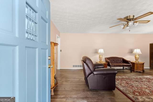 living room with dark hardwood / wood-style flooring, ceiling fan, and a textured ceiling