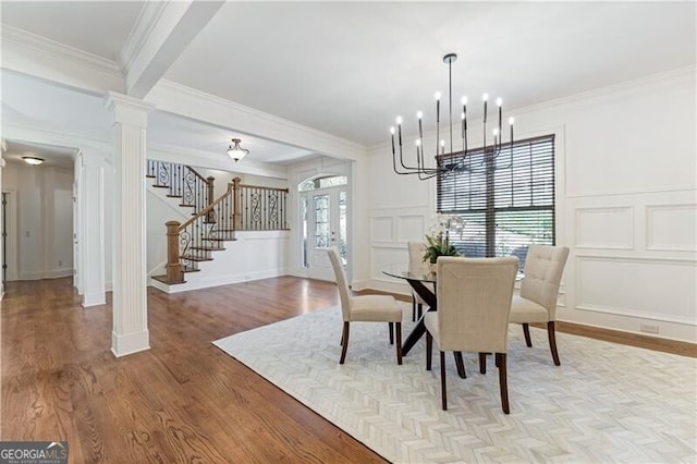 dining room featuring an inviting chandelier, light hardwood / wood-style flooring, crown molding, and ornate columns