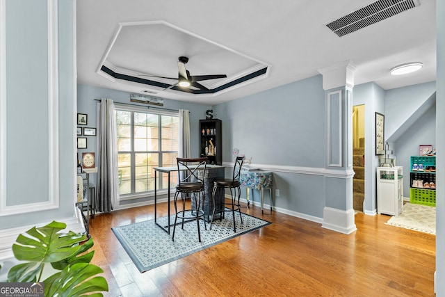 dining room featuring light wood-type flooring, a tray ceiling, ceiling fan, and decorative columns