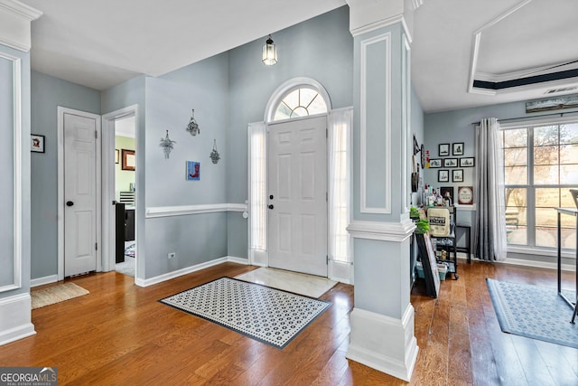 entrance foyer with wood-type flooring, decorative columns, a tray ceiling, and crown molding