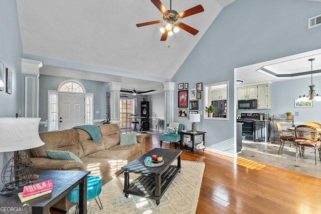 living room featuring a high ceiling, light hardwood / wood-style floors, ceiling fan, and decorative columns