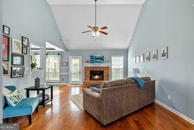 living room featuring hardwood / wood-style flooring, ceiling fan, a high ceiling, and a brick fireplace