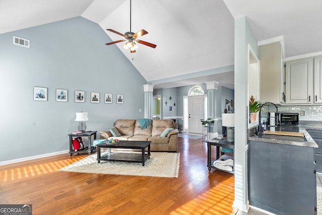 living room with ornate columns, ceiling fan, sink, wood-type flooring, and high vaulted ceiling