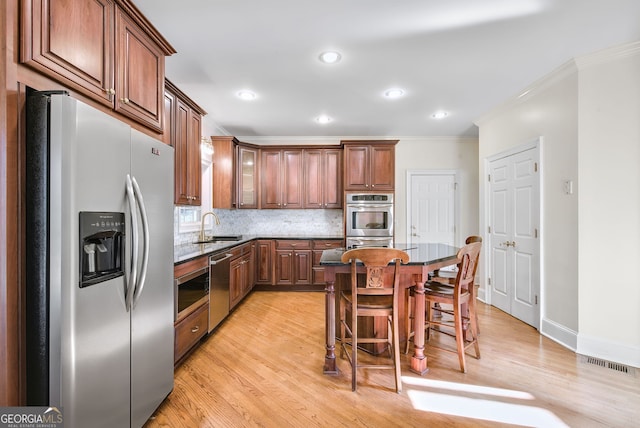 kitchen with a center island, crown molding, light hardwood / wood-style floors, decorative backsplash, and appliances with stainless steel finishes