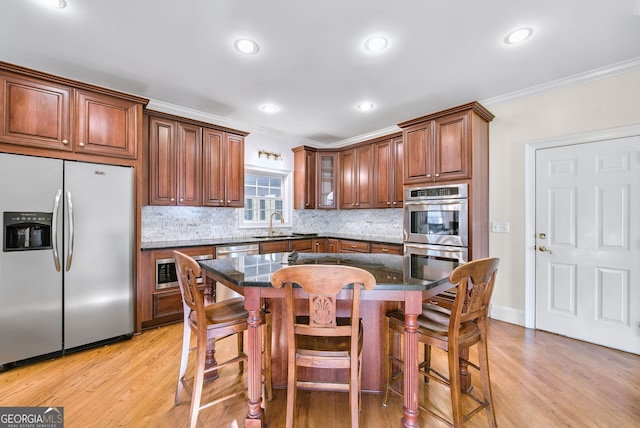 kitchen featuring stainless steel appliances, a kitchen breakfast bar, light hardwood / wood-style flooring, dark stone countertops, and a kitchen island