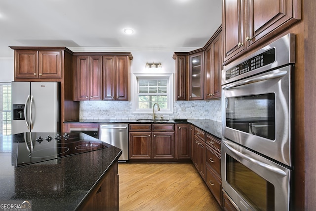 kitchen featuring dark stone countertops, sink, light wood-type flooring, and appliances with stainless steel finishes