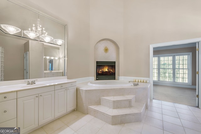 bathroom with tile patterned floors, vanity, tiled tub, an inviting chandelier, and a high ceiling