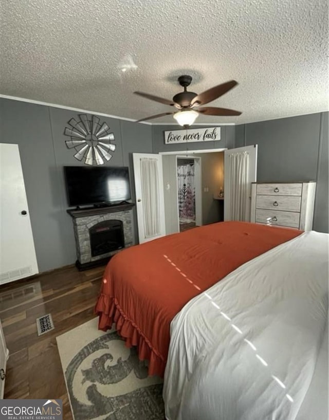 bedroom with a textured ceiling, ceiling fan, a fireplace, and dark hardwood / wood-style floors