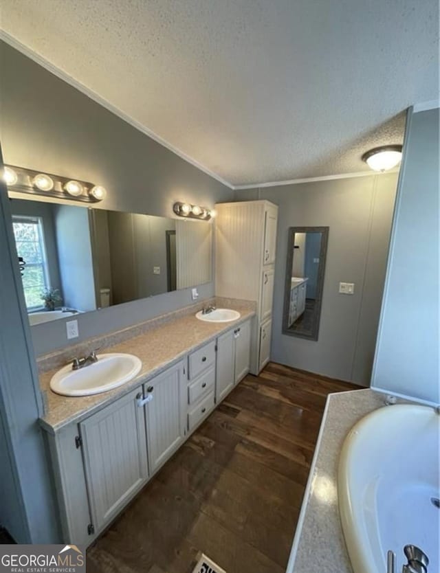 bathroom with hardwood / wood-style floors, vanity, ornamental molding, a tub to relax in, and a textured ceiling