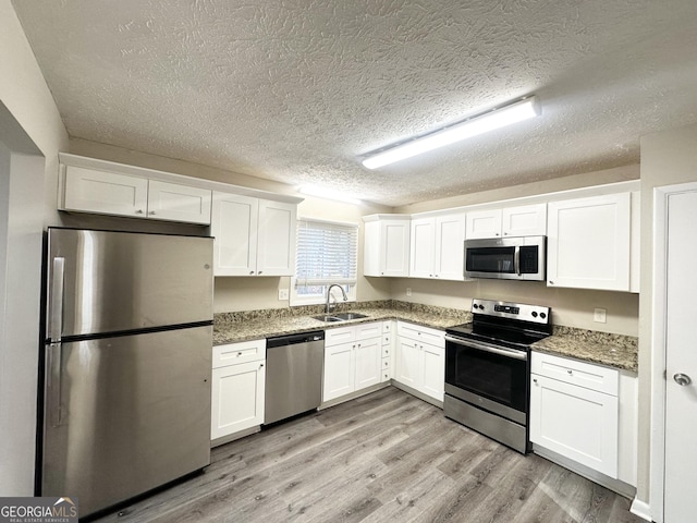 kitchen with appliances with stainless steel finishes, light wood-type flooring, dark stone counters, sink, and white cabinetry