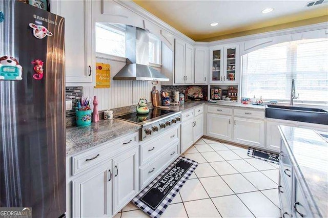 kitchen with sink, wall chimney range hood, stainless steel fridge, black electric cooktop, and white cabinets