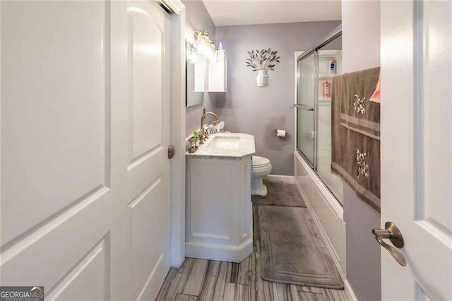 full bathroom featuring hardwood / wood-style floors, vanity, toilet, and bath / shower combo with glass door