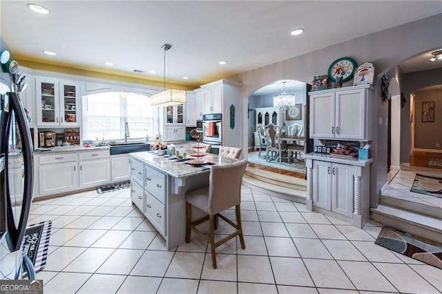 kitchen featuring stainless steel refrigerator, white cabinetry, a kitchen island, and hanging light fixtures