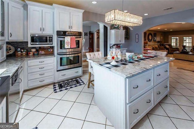 kitchen featuring backsplash, stainless steel appliances, light tile patterned floors, decorative light fixtures, and white cabinets