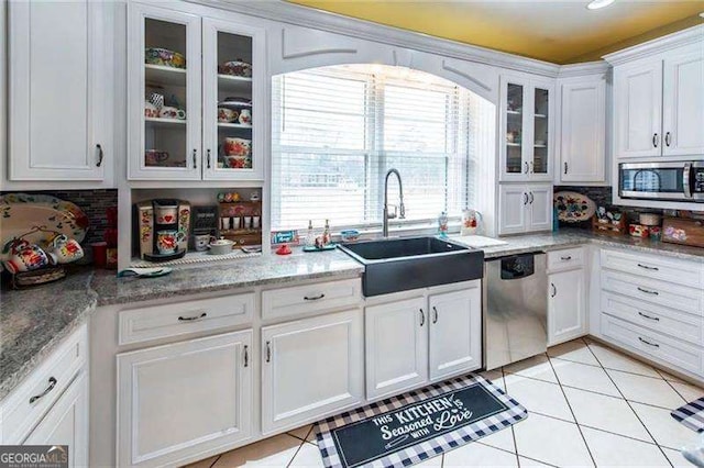 kitchen featuring decorative backsplash, stainless steel appliances, sink, light tile patterned floors, and white cabinets