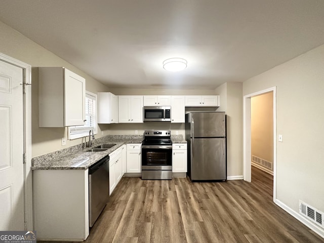 kitchen with stone counters, sink, appliances with stainless steel finishes, white cabinets, and hardwood / wood-style flooring