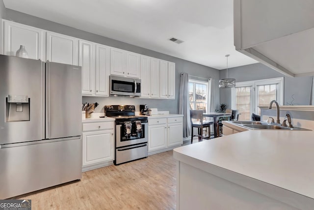 kitchen featuring white cabinetry, sink, stainless steel appliances, light hardwood / wood-style flooring, and decorative light fixtures