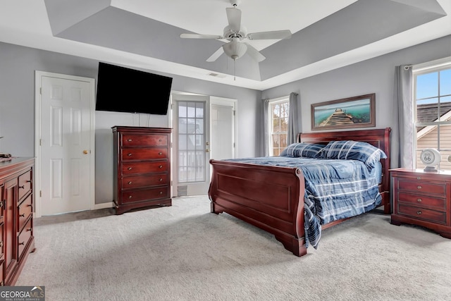 bedroom with light colored carpet, a raised ceiling, and ceiling fan