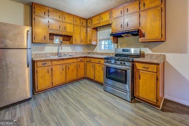 kitchen featuring a textured ceiling, sink, light wood-type flooring, and stainless steel appliances