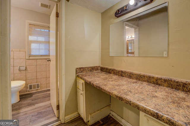 bathroom with wood-type flooring, vanity, toilet, and tile walls