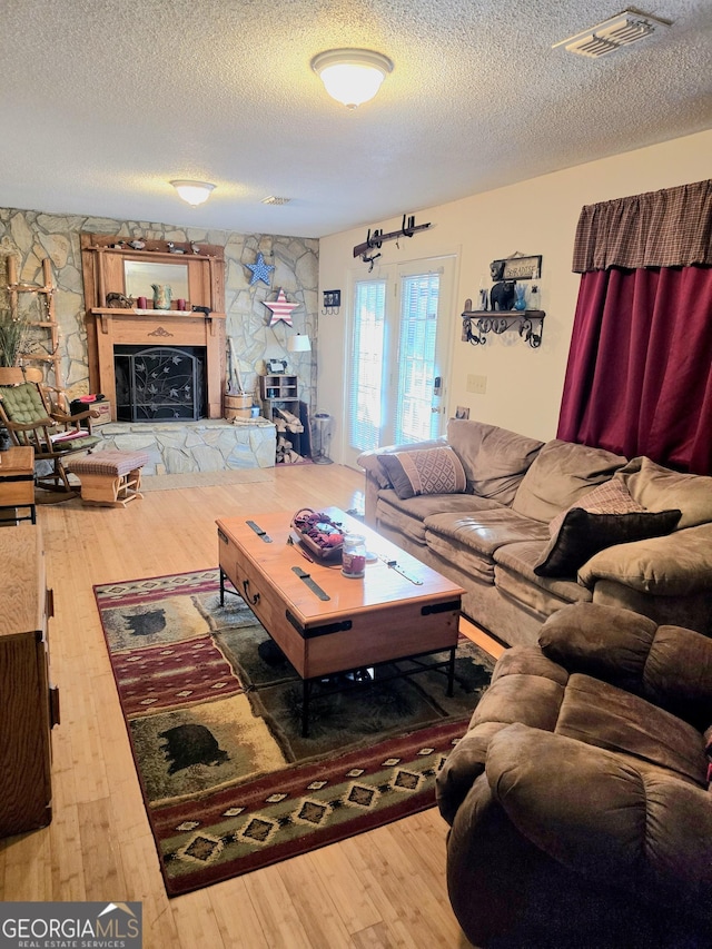 living room with hardwood / wood-style flooring, a stone fireplace, and a textured ceiling