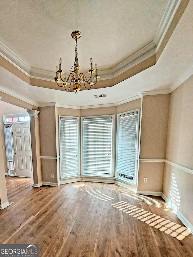 spare room with a tray ceiling, crown molding, hardwood / wood-style flooring, and an inviting chandelier