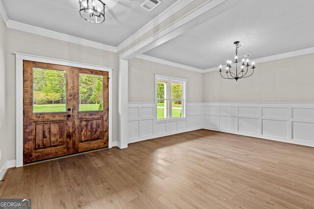 foyer entrance with a notable chandelier, wood-type flooring, crown molding, and a wealth of natural light