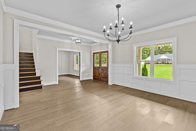 unfurnished dining area with a wealth of natural light, french doors, an inviting chandelier, light hardwood / wood-style floors, and ornamental molding