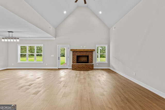 unfurnished living room with a high ceiling, light hardwood / wood-style flooring, a brick fireplace, and ceiling fan