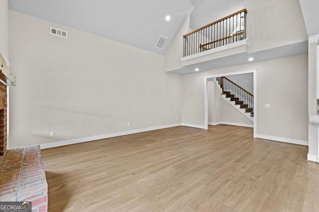 unfurnished living room with a high ceiling, light hardwood / wood-style flooring, and a brick fireplace