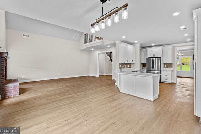 kitchen featuring stainless steel refrigerator, kitchen peninsula, pendant lighting, white cabinets, and light wood-type flooring