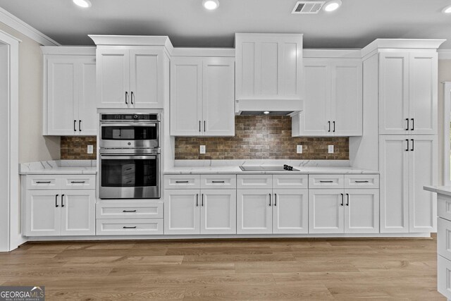 kitchen with light wood-type flooring, white cabinetry, extractor fan, and double oven